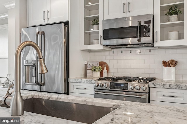 kitchen with light stone countertops, white cabinetry, stainless steel appliances, and tasteful backsplash