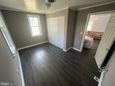 unfurnished bedroom featuring crown molding, a closet, and dark wood-type flooring