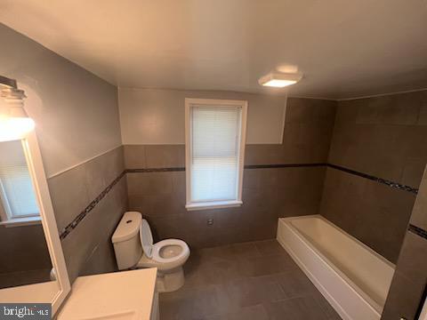 bathroom with a washtub, vanity, tile walls, and toilet