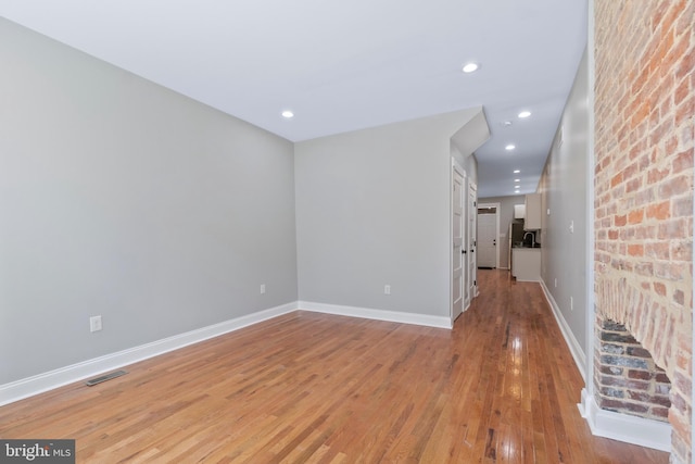 unfurnished room featuring brick wall and light wood-type flooring