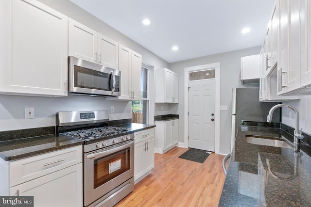 kitchen featuring appliances with stainless steel finishes, sink, dark stone countertops, white cabinets, and light hardwood / wood-style floors