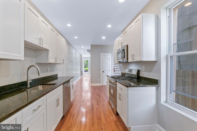 kitchen featuring appliances with stainless steel finishes, sink, dark stone countertops, light hardwood / wood-style floors, and white cabinetry