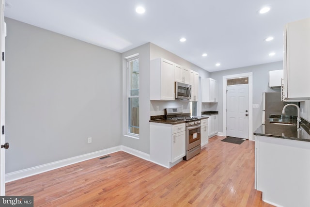 kitchen with dark stone counters, white cabinets, sink, light wood-type flooring, and appliances with stainless steel finishes