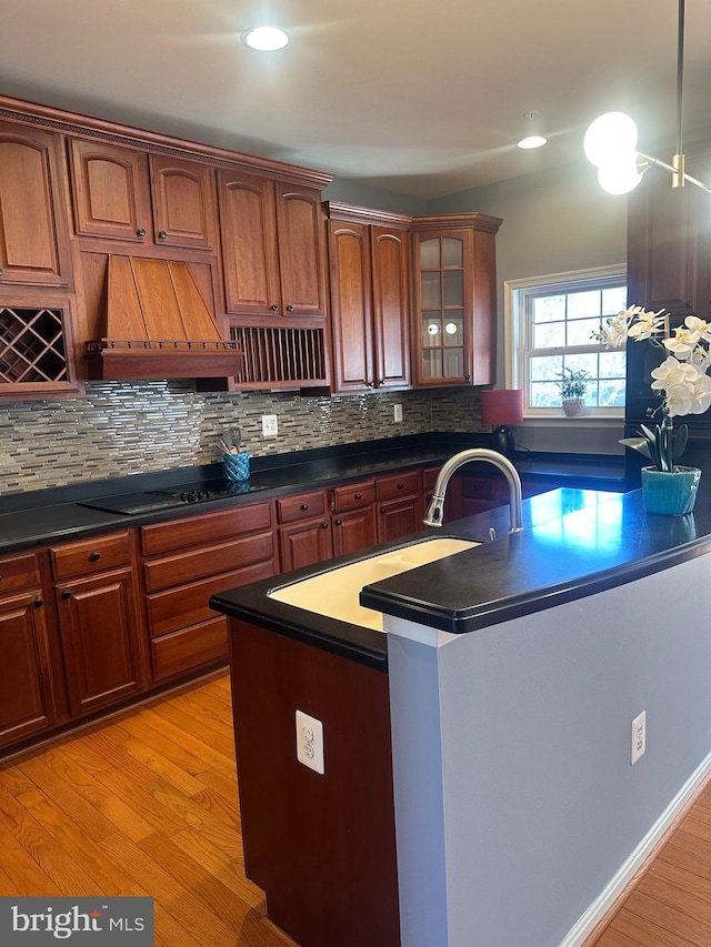 kitchen with black electric cooktop, custom exhaust hood, tasteful backsplash, and light wood-type flooring