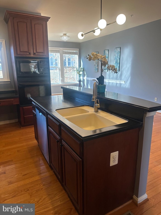 kitchen featuring sink, light wood-type flooring, black appliances, and a center island with sink