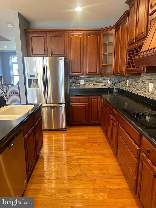 kitchen featuring sink, custom range hood, stainless steel appliances, light hardwood / wood-style floors, and decorative backsplash