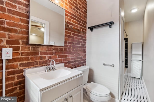 bathroom featuring vanity, brick wall, and toilet