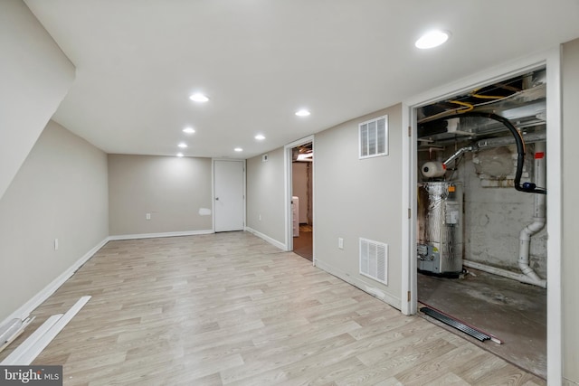 basement featuring electric water heater and light hardwood / wood-style floors