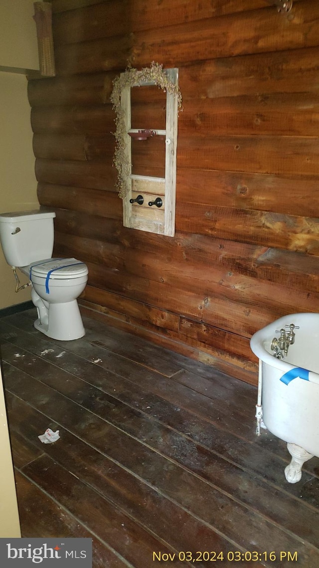 bathroom with a washtub, hardwood / wood-style floors, log walls, and toilet