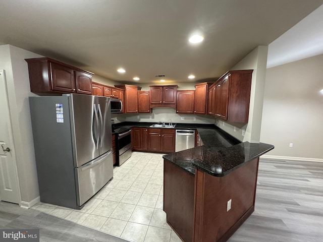 kitchen with dark stone counters, sink, appliances with stainless steel finishes, light hardwood / wood-style floors, and kitchen peninsula