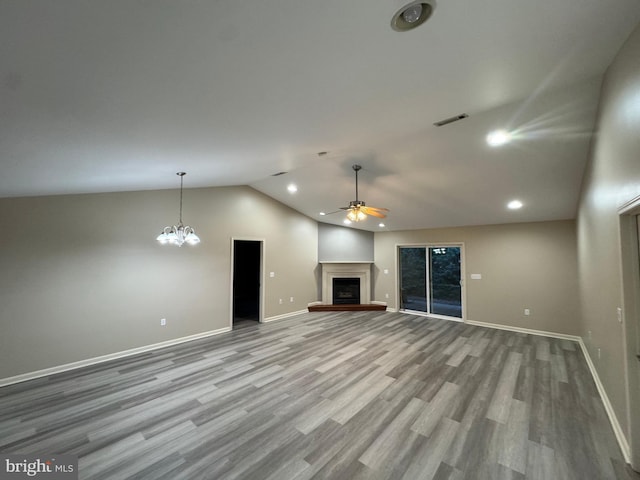 unfurnished living room with ceiling fan with notable chandelier, vaulted ceiling, and light hardwood / wood-style flooring