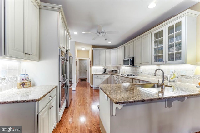 kitchen featuring appliances with stainless steel finishes, sink, kitchen peninsula, light hardwood / wood-style flooring, and a breakfast bar area