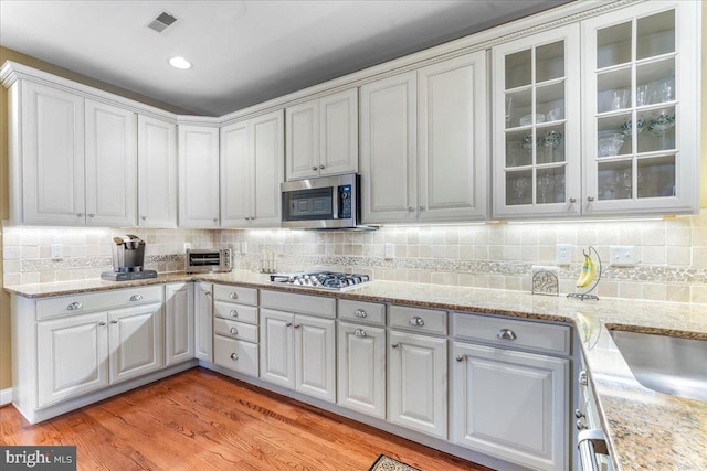 kitchen with white cabinetry, appliances with stainless steel finishes, light hardwood / wood-style flooring, and tasteful backsplash