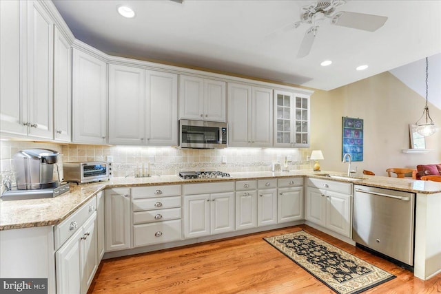 kitchen with pendant lighting, kitchen peninsula, sink, white cabinetry, and stainless steel appliances