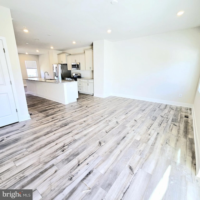 kitchen featuring a kitchen island with sink, white cabinets, sink, light hardwood / wood-style floors, and stainless steel appliances