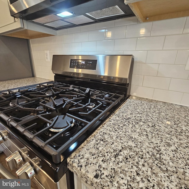 details with stainless steel gas range oven, light stone countertops, decorative backsplash, and ventilation hood