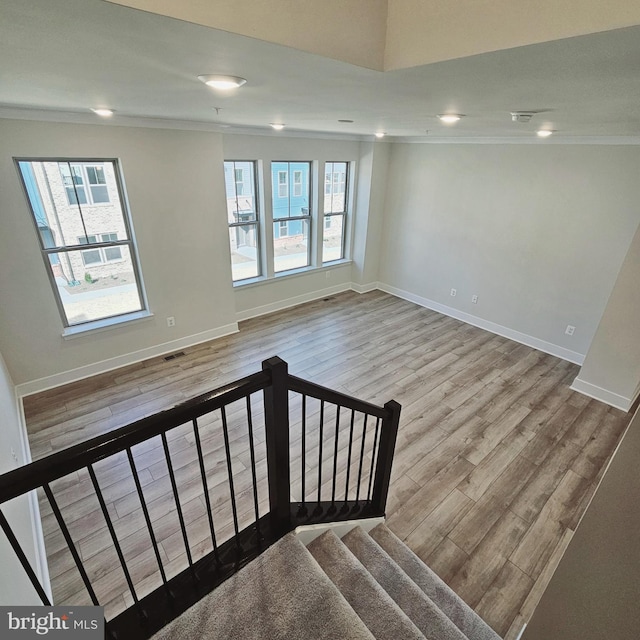 stairway with wood-type flooring, a wealth of natural light, and ornamental molding