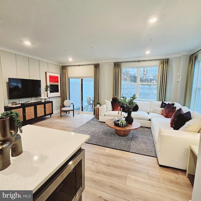 living room with a healthy amount of sunlight, ornamental molding, and light hardwood / wood-style flooring