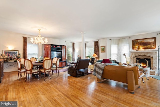 living room featuring an inviting chandelier, light hardwood / wood-style flooring, a brick fireplace, and a healthy amount of sunlight