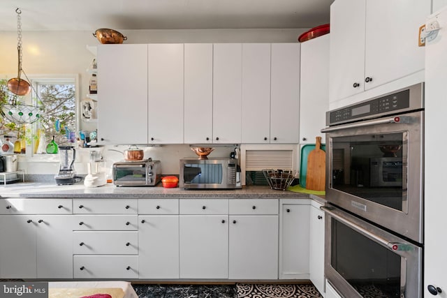 kitchen with decorative light fixtures, stainless steel appliances, and white cabinetry