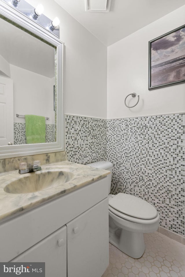 bathroom with toilet, vanity, tile patterned floors, and tile walls