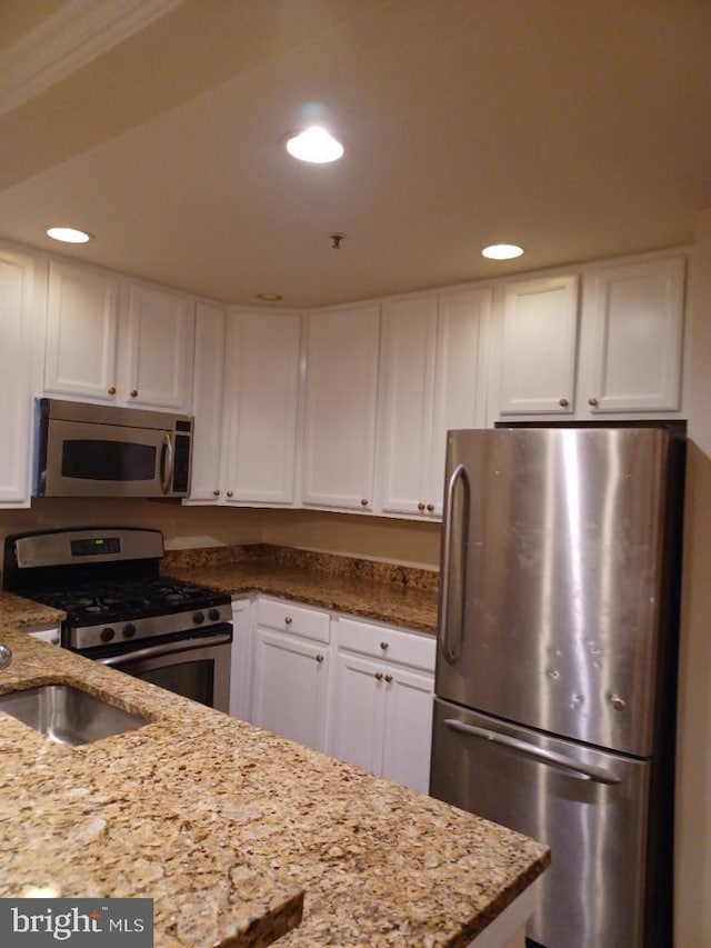 kitchen featuring light stone countertops, appliances with stainless steel finishes, white cabinetry, and crown molding