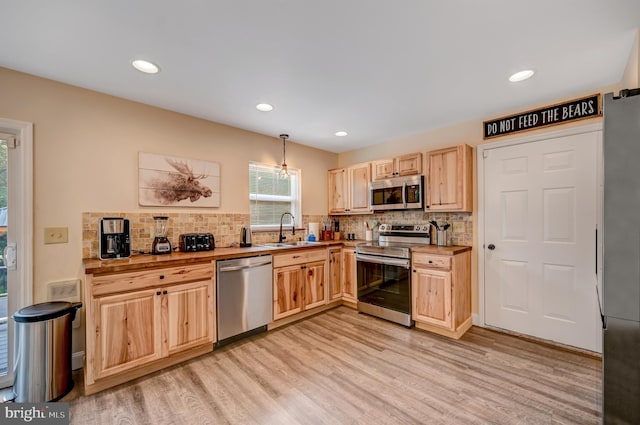 kitchen with sink, hanging light fixtures, butcher block countertops, appliances with stainless steel finishes, and light wood-type flooring