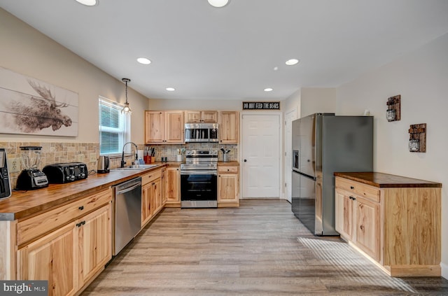 kitchen featuring light wood-type flooring, wooden counters, decorative light fixtures, and appliances with stainless steel finishes