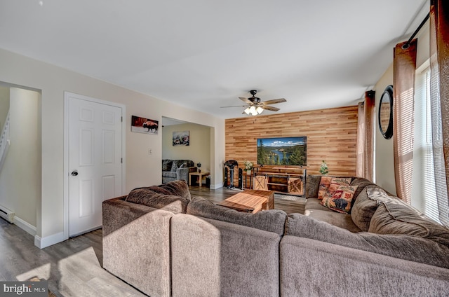 living room featuring wood walls, ceiling fan, light hardwood / wood-style floors, and a baseboard heating unit