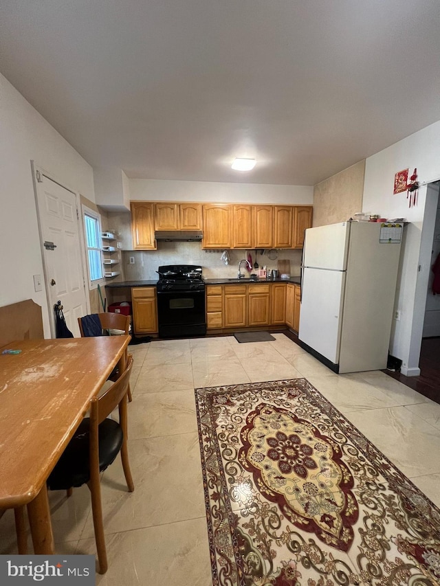 kitchen with tasteful backsplash, black gas range oven, sink, light tile patterned floors, and white fridge