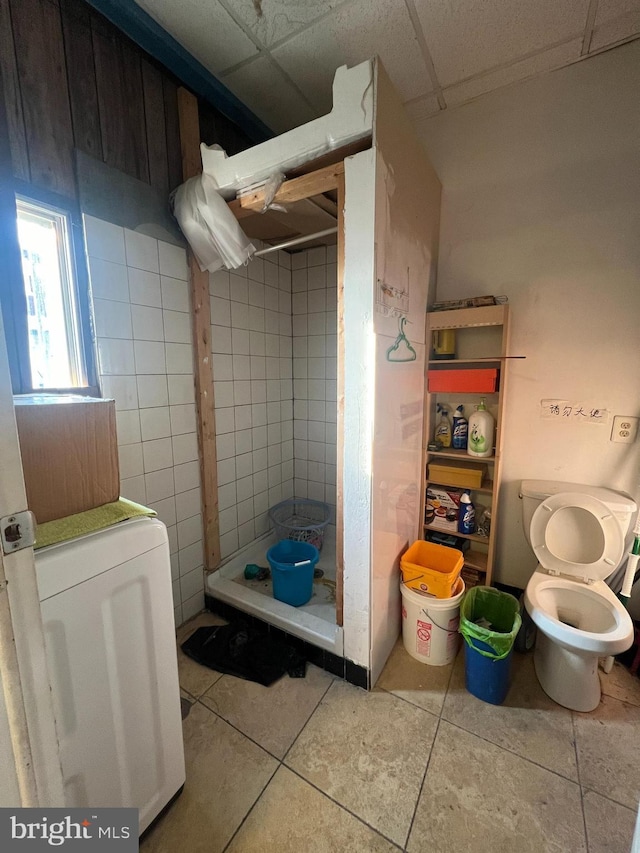 bathroom with tile patterned flooring, a drop ceiling, toilet, and washer / clothes dryer