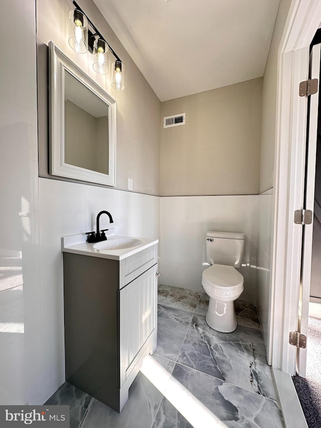 bathroom featuring vanity, toilet, and tile walls