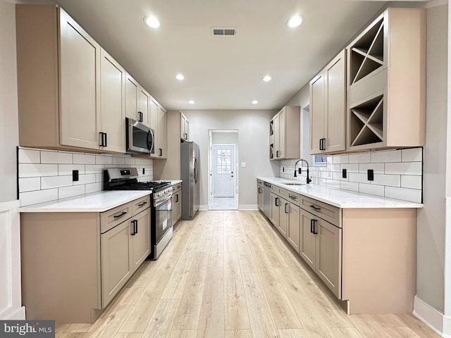 kitchen with appliances with stainless steel finishes, light hardwood / wood-style floors, gray cabinetry, and sink