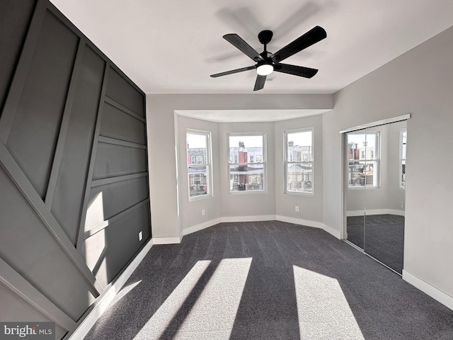 unfurnished bedroom with ceiling fan and dark colored carpet