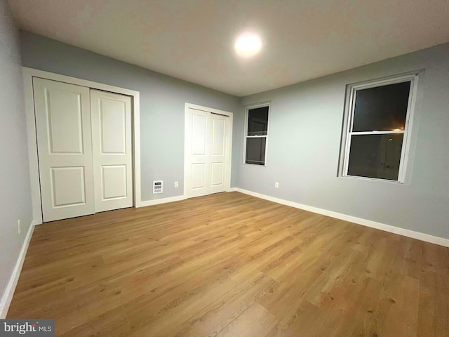 unfurnished bedroom featuring multiple closets and light hardwood / wood-style flooring