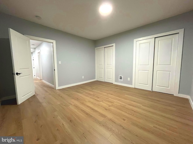 unfurnished bedroom with light hardwood / wood-style floors and multiple closets