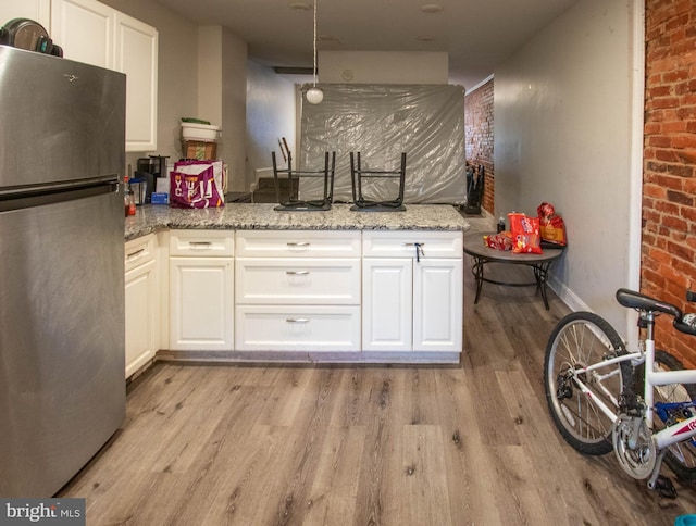 kitchen featuring white cabinets, stainless steel fridge, and brick wall