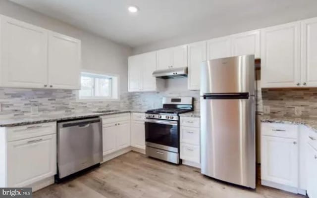 kitchen featuring white cabinets, decorative backsplash, light stone countertops, light wood-type flooring, and appliances with stainless steel finishes