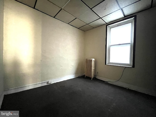 empty room with carpet flooring, a paneled ceiling, and radiator heating unit