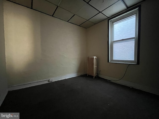 carpeted spare room featuring a paneled ceiling and radiator heating unit