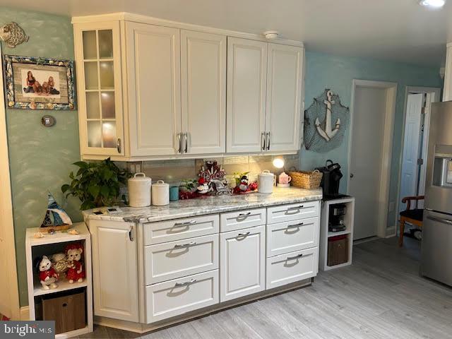 kitchen featuring white cabinets, stainless steel fridge, light stone counters, and light wood-type flooring