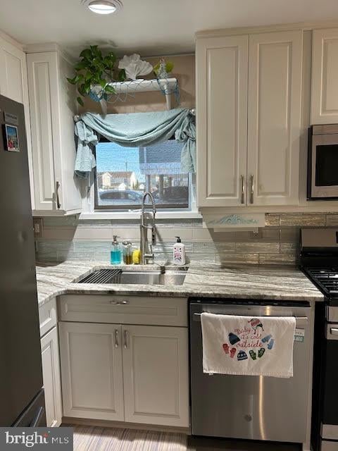 kitchen with white cabinets, stainless steel appliances, light stone counters, and sink