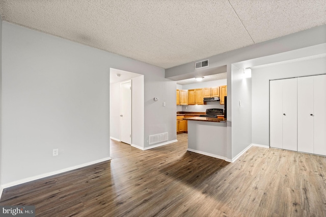 kitchen featuring kitchen peninsula, black stove, a textured ceiling, and hardwood / wood-style flooring