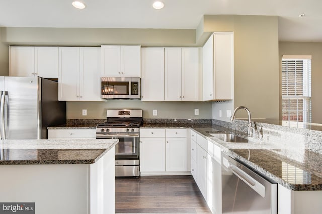 kitchen with appliances with stainless steel finishes, white cabinetry, dark stone counters, and sink