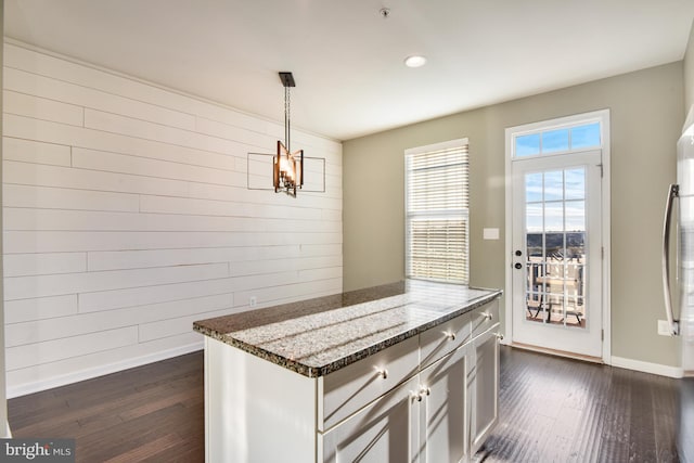 kitchen with stone counters, hanging light fixtures, dark wood-type flooring, and wood walls