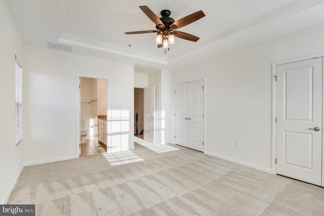 unfurnished bedroom featuring ceiling fan, light colored carpet, multiple windows, and a tray ceiling