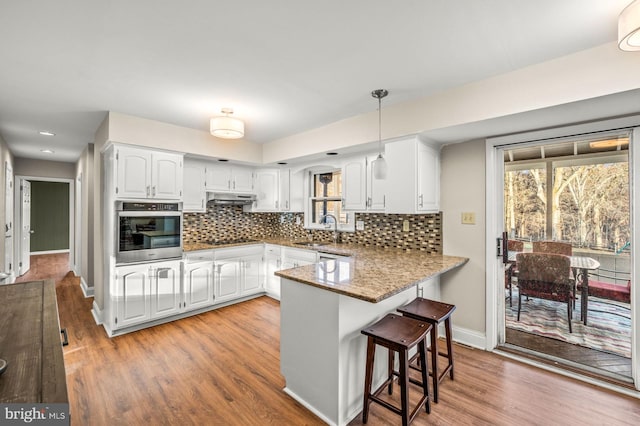 kitchen featuring stainless steel oven, light hardwood / wood-style flooring, kitchen peninsula, decorative light fixtures, and white cabinets