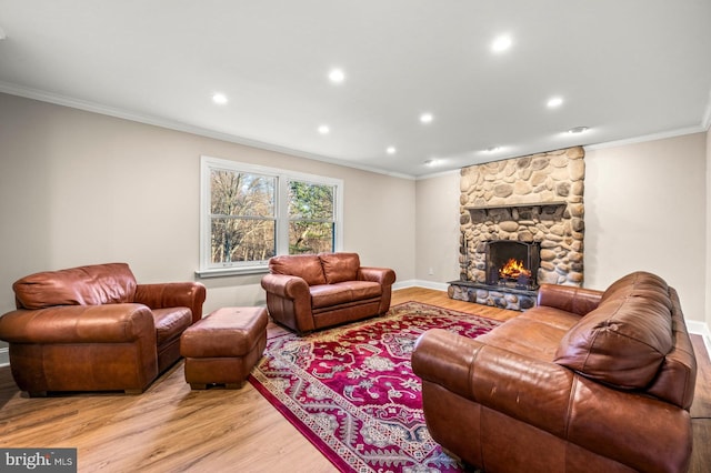 living room with a stone fireplace, ornamental molding, and light wood-type flooring