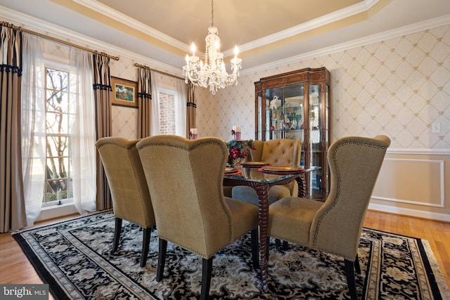 dining space featuring a raised ceiling, wood-type flooring, a notable chandelier, and ornamental molding