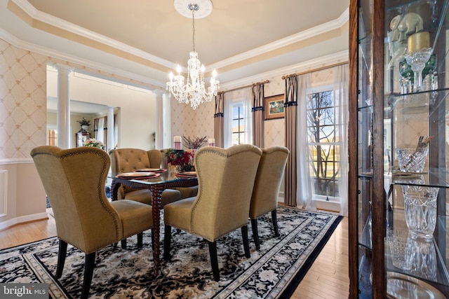 dining area featuring hardwood / wood-style floors, ornate columns, ornamental molding, and an inviting chandelier